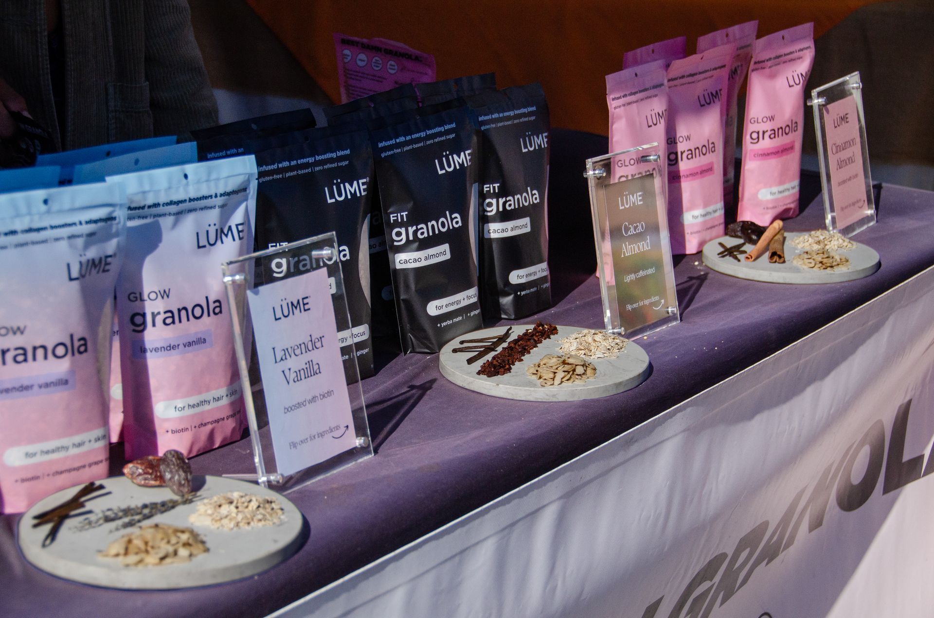 A display table featuring various bags of Lume granola, informational signs, and small plates with ingredient samples.