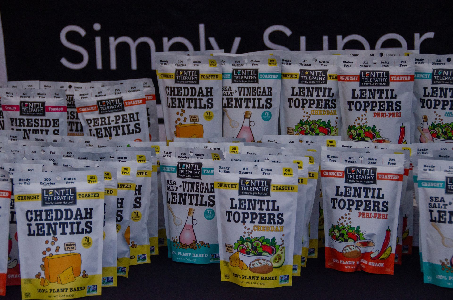 Many pouches of Simply Super Lentil Toppers and Lentils in various flavors, arranged on a dark table.