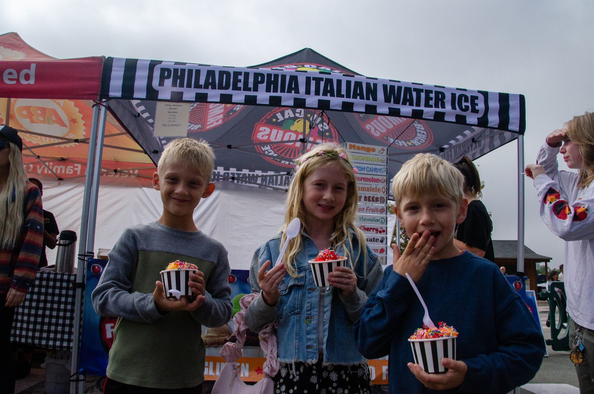 Three children eating treats in paper cups under a 