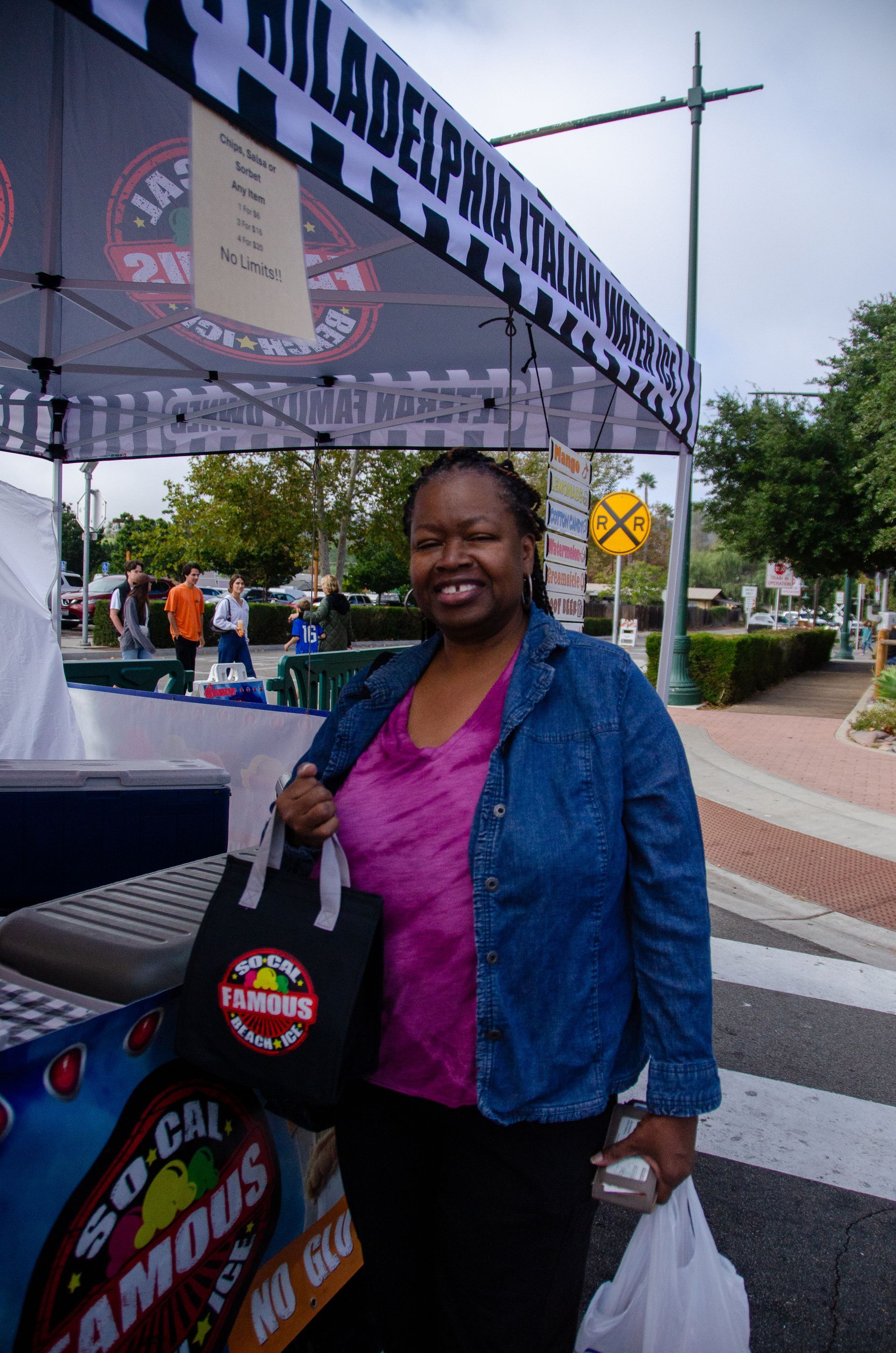 A person smiles while standing at a food tent labeled 