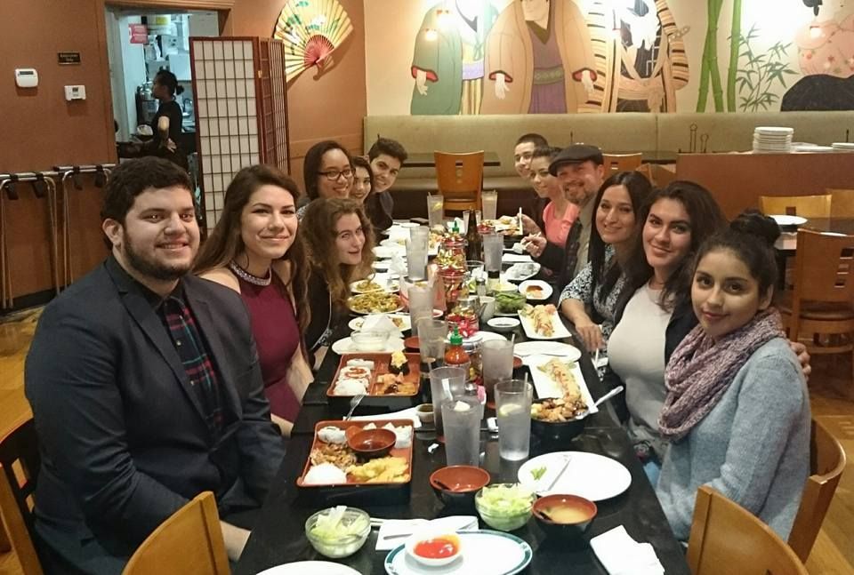 A group of people dining together at a restaurant with Japanese-themed decor, sitting at a long, food-filled table.