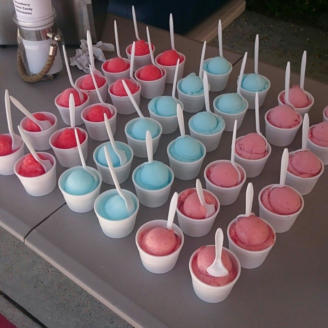 A table with many small white cups of blue and pink sorbet, each containing a white plastic spoon.
