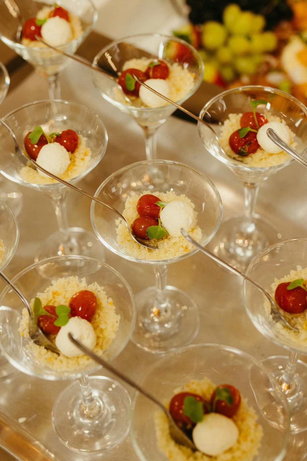 A high-angle view of several martini glasses filled with couscous, cherry tomatoes, and mozzarella balls as appetizers.