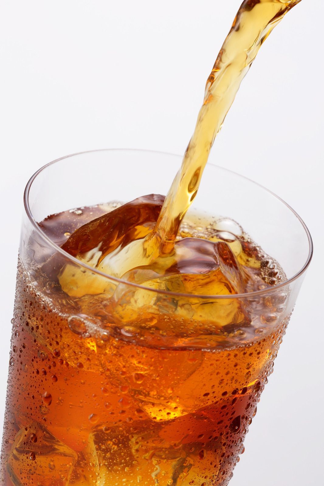 Iced beverage being poured into a glass filled with ice cubes, amber liquid and condensation visible.