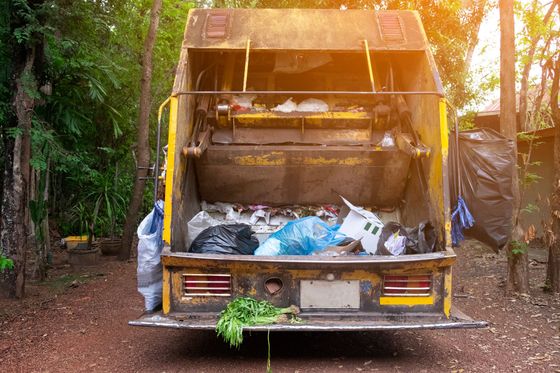 A crane is lifting a bucket of garbage into a dumpster.