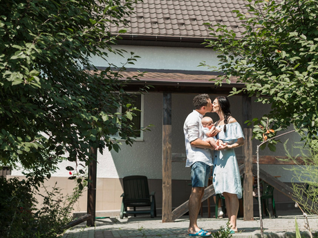 Family of three standing outside a house, holding a baby under the porch in front of the door.