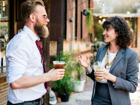 Two people chatting outside a café, each holding iced drinks, smiling and gesturing.