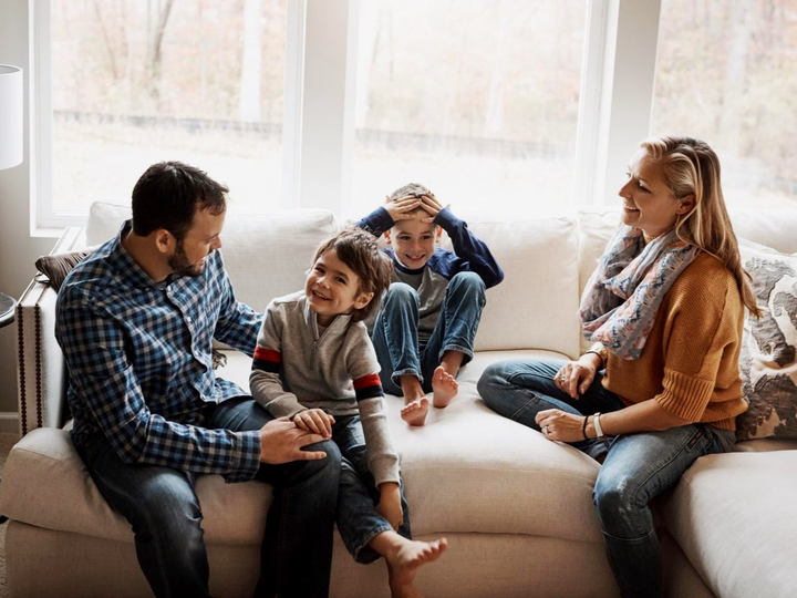 Four people sit together on a couch in a bright living room, chatting and smiling.