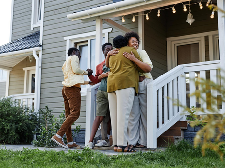 Friends hugging on a house porch with moving boxes and string lights