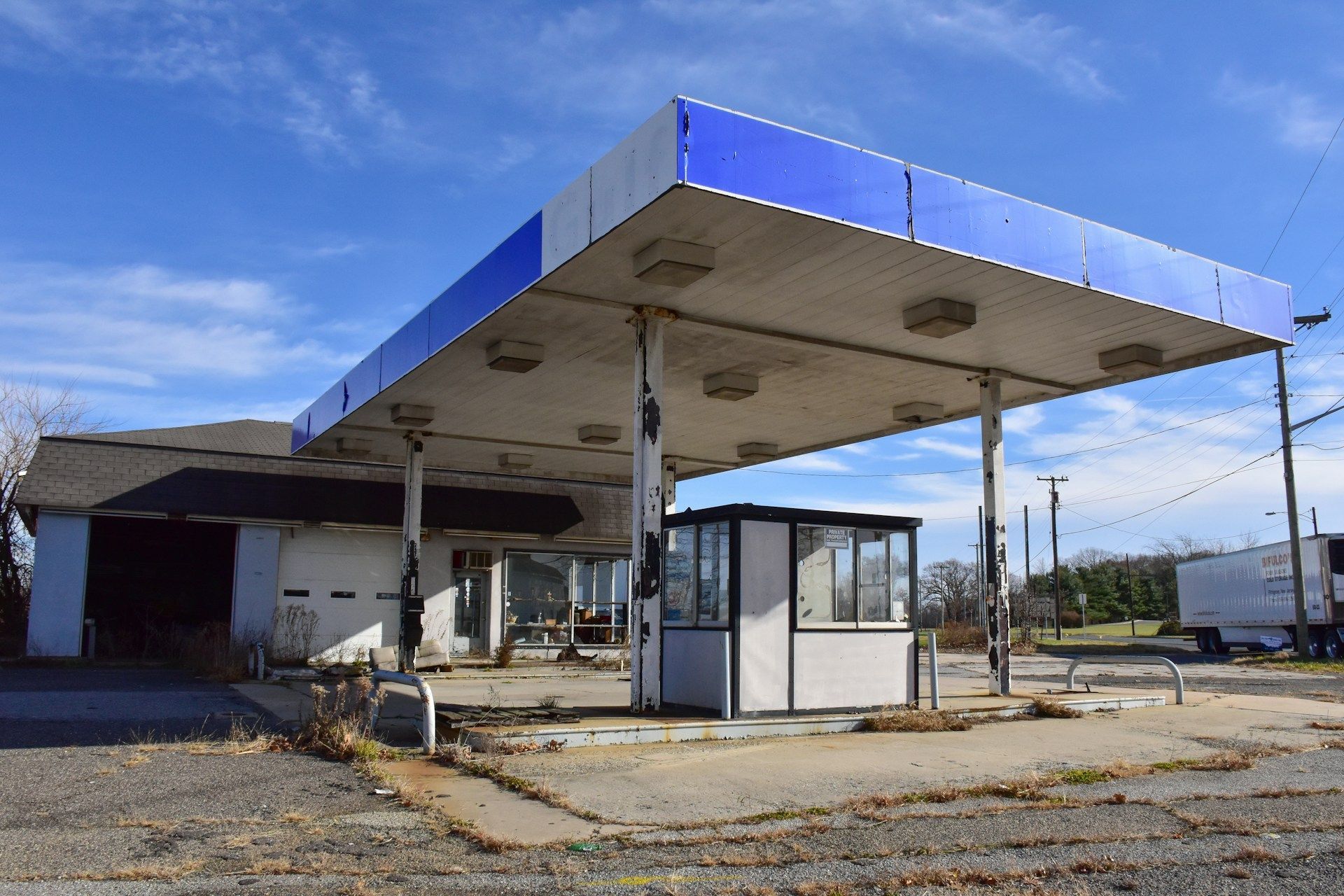 Abandoned gas station with a blue canopy and small white booth under a clear sky