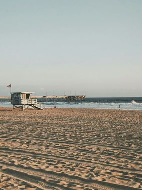 Lifeguard stand on sandy beach with a pier in the distance; blue ocean and sky.
