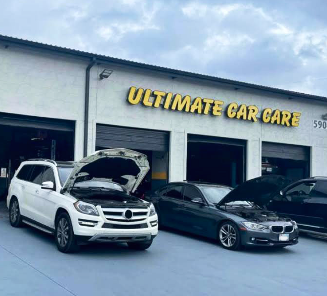 A white SUV and a dark gray sedan with their hoods open parked in front of an Ultimate Car Care auto shop.