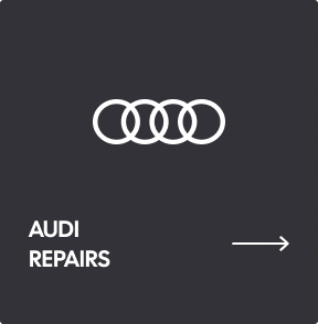 A dark grey directional sign featuring the white Audi logo, the text 