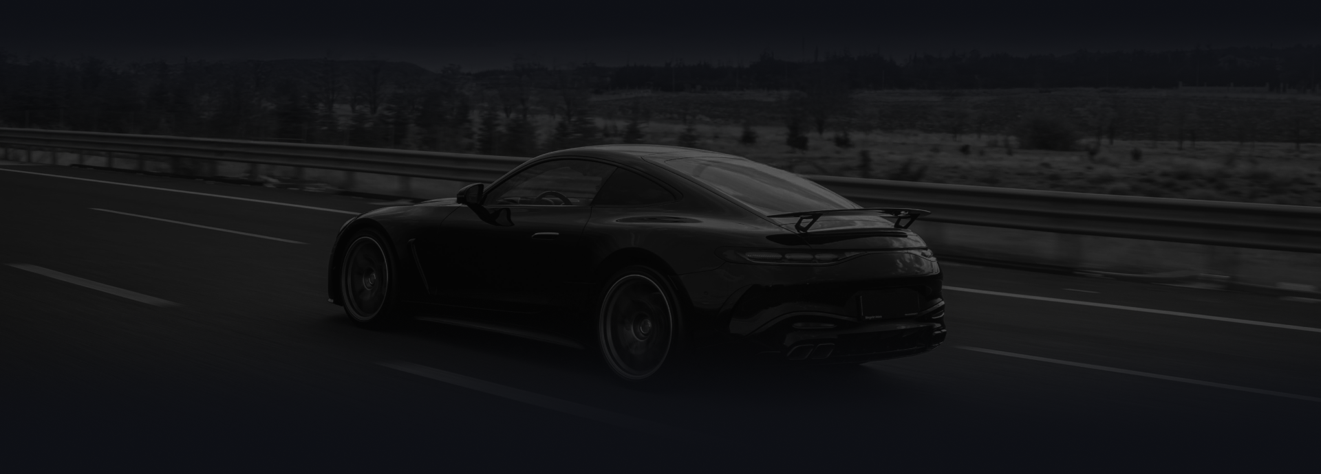 A dark-colored sports car driving on a highway at twilight.