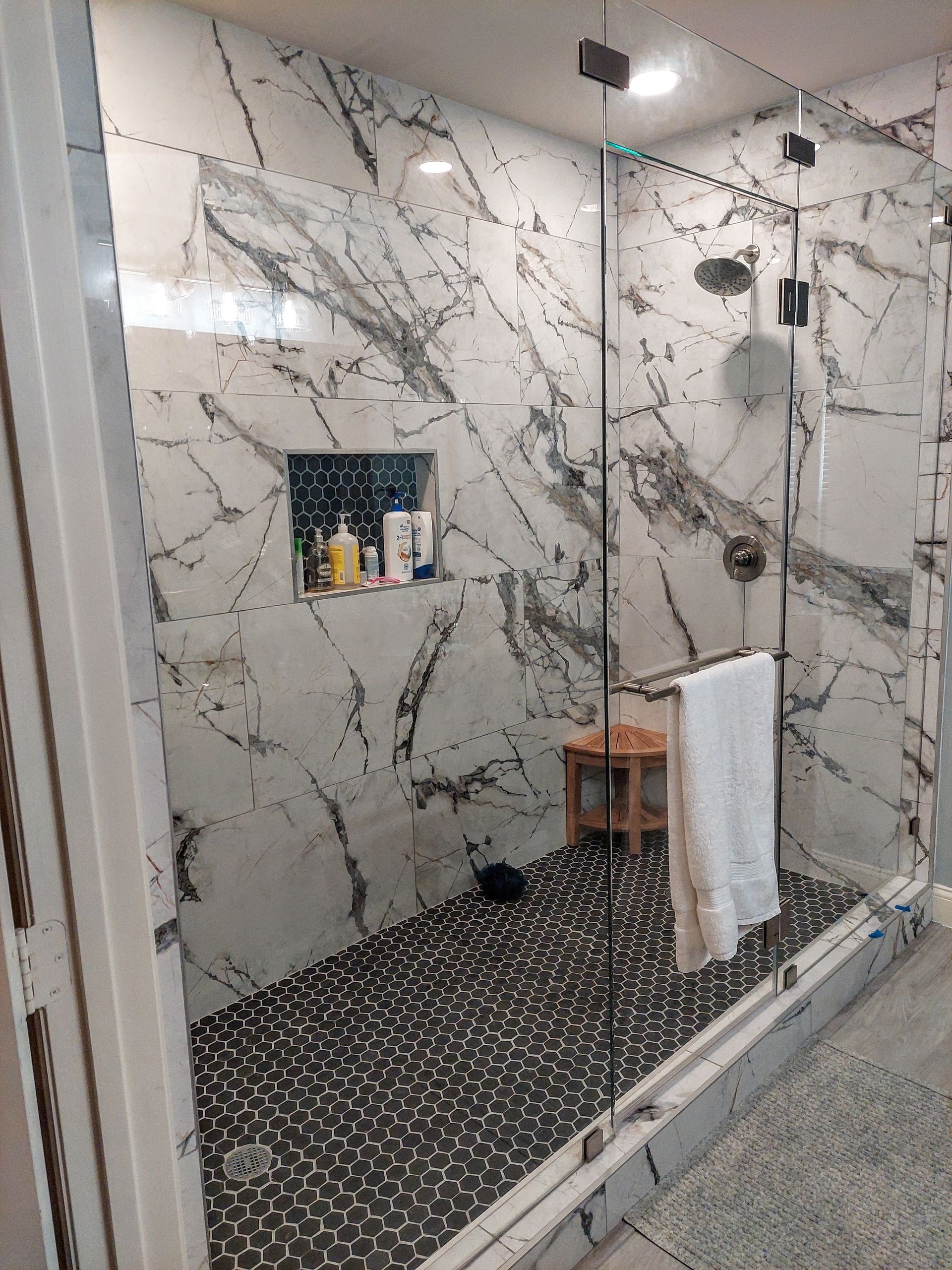 a bathroom with marble walls and a walk in shower with a glass door .