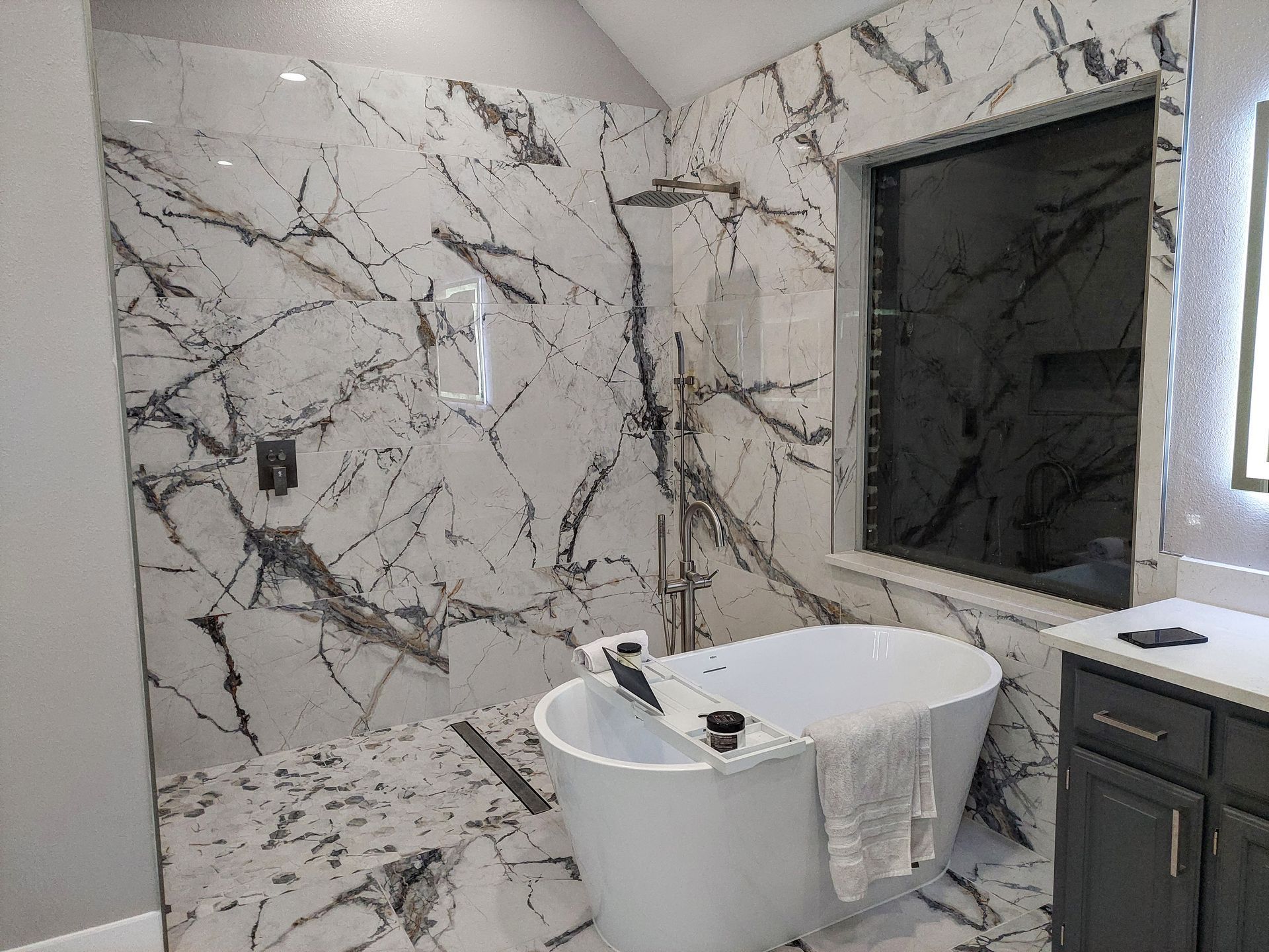 a bathroom with marble tiles , a tub , a shower and a window .