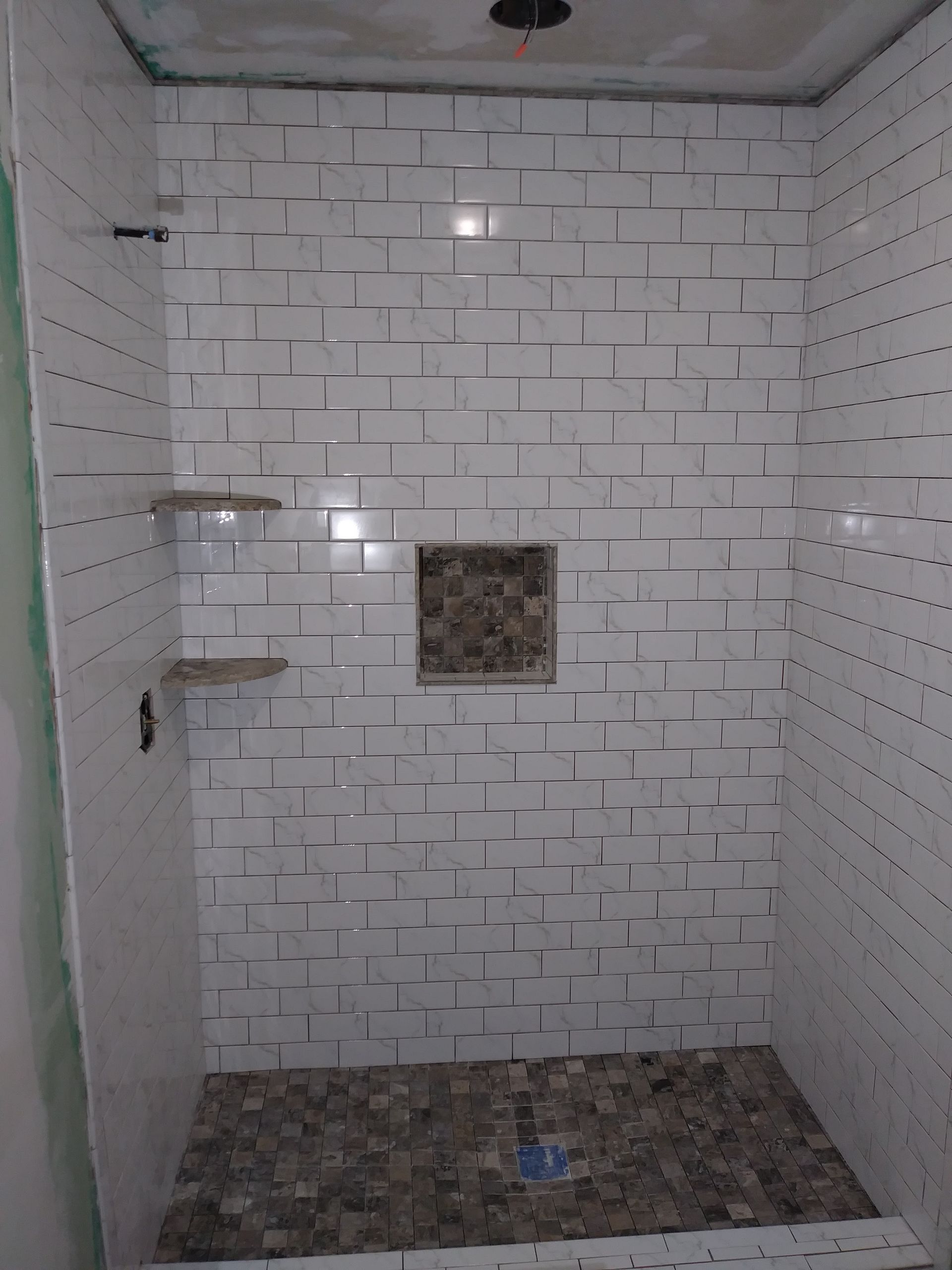 a shower stall with white tiles and a mosaic floor .