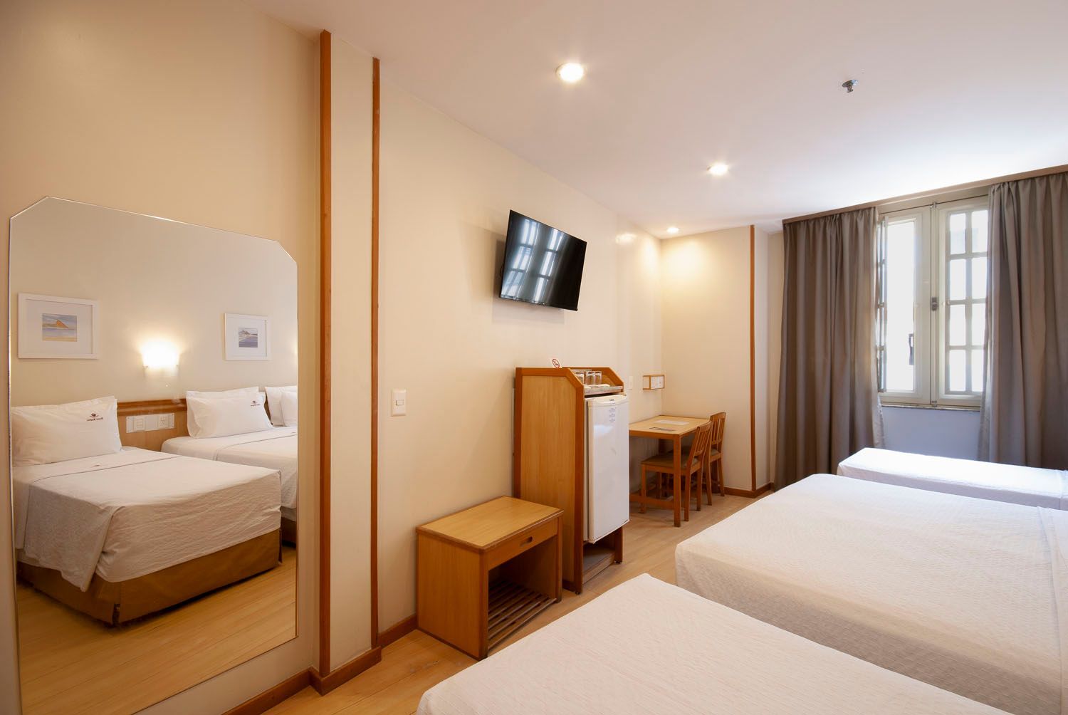 Um quarto de hotel com duas camas, uma escrivaninha, uma televisão e um espelho.