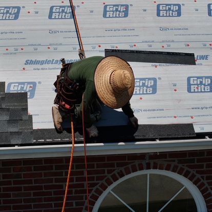 A man wearing a straw hat is working on a roof with grip rite shingles