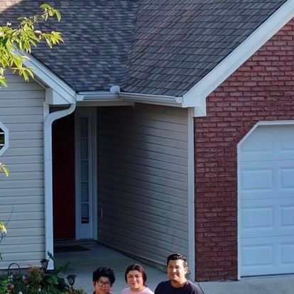 A man and two women are standing in front of a brick house.