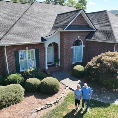 A man and a woman are standing in front of a brick house.