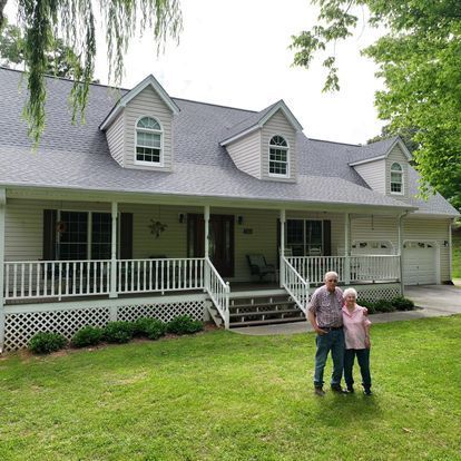 A man and a woman are standing in front of a house.