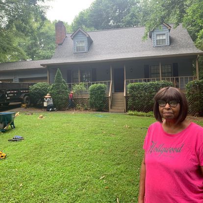 A woman in a pink hollywood shirt stands in front of a house