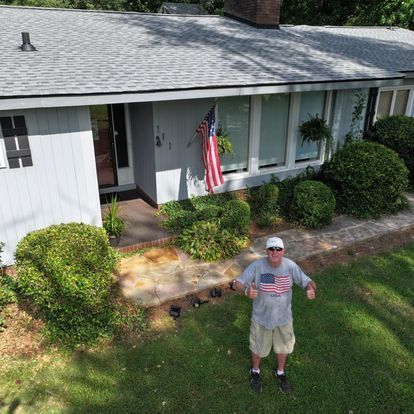 A man in an american flag shirt is standing in front of a house