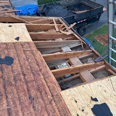 The roof of a house is being demolished and a dump truck is parked in the background.