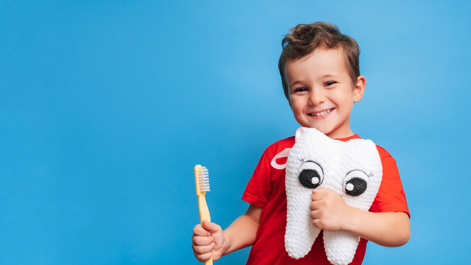 A boy with healthy teeth holds a plush tooth and tooth brush after a dental checkup