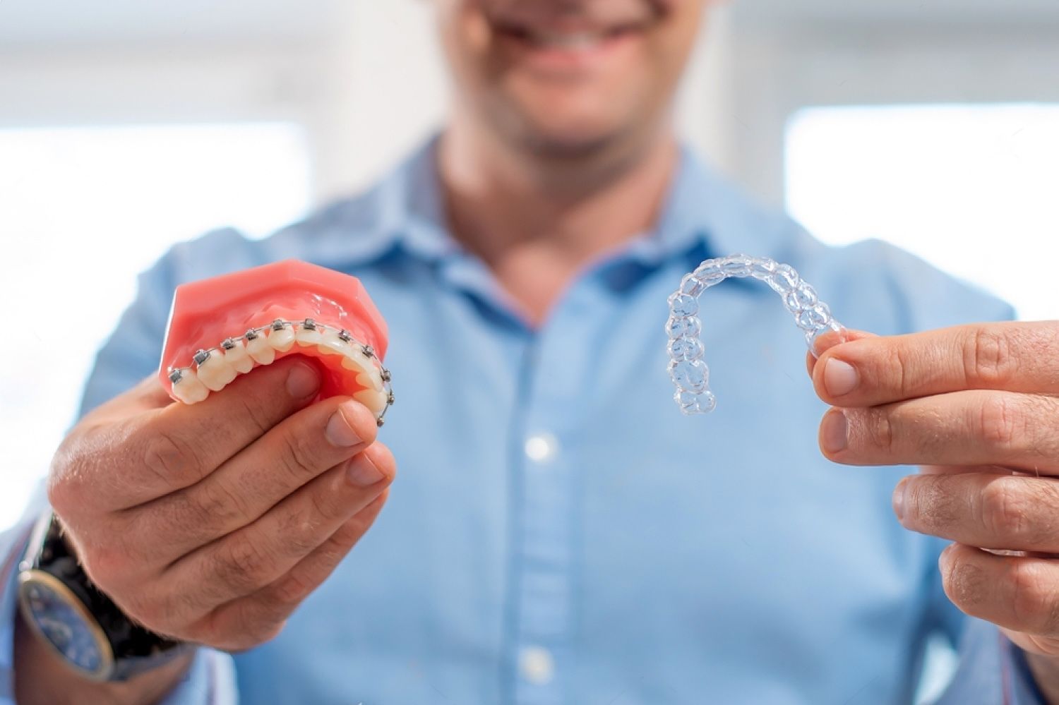 smiling dentist holding aligners and braces in hand shows the difference