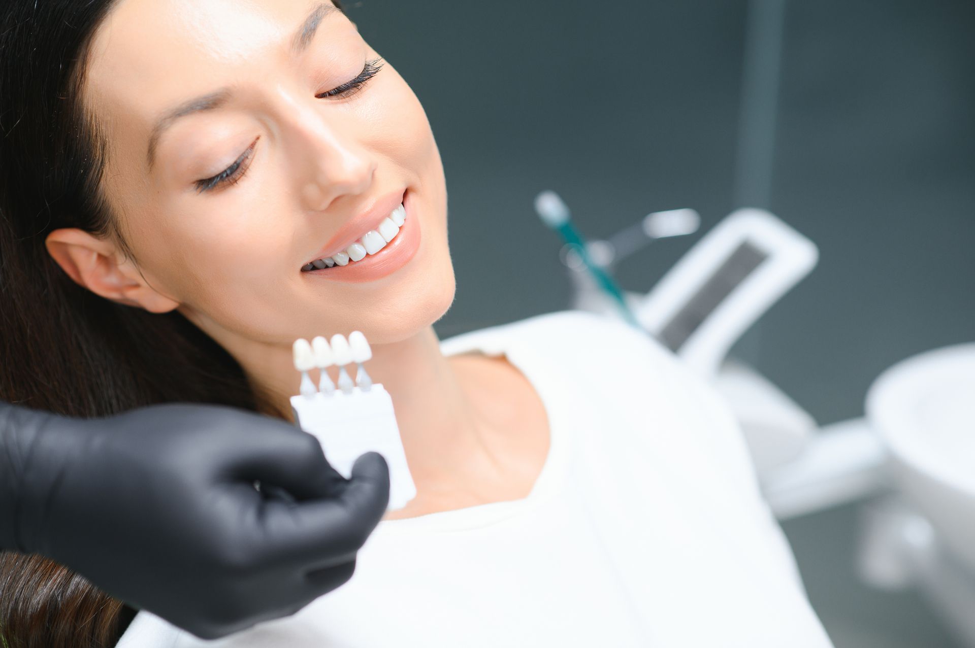 Smiling woman holding a teeth shade guide, showing her 5x whiter smile after teeth whitening