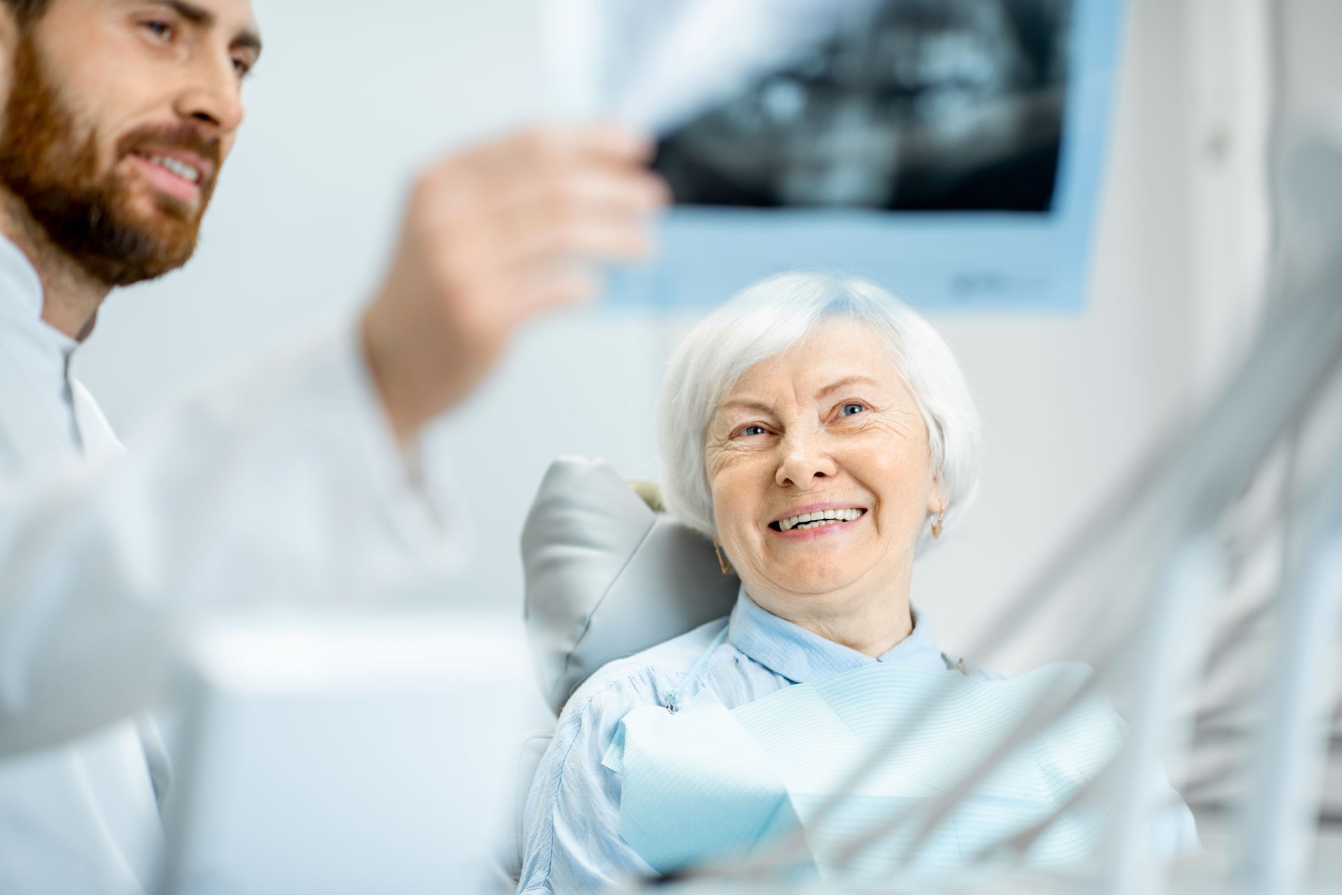 Elderly woman smiling in a dental chair while a dentist shows her a dental X-ray, during a dental implant check-up in Toowoomba.