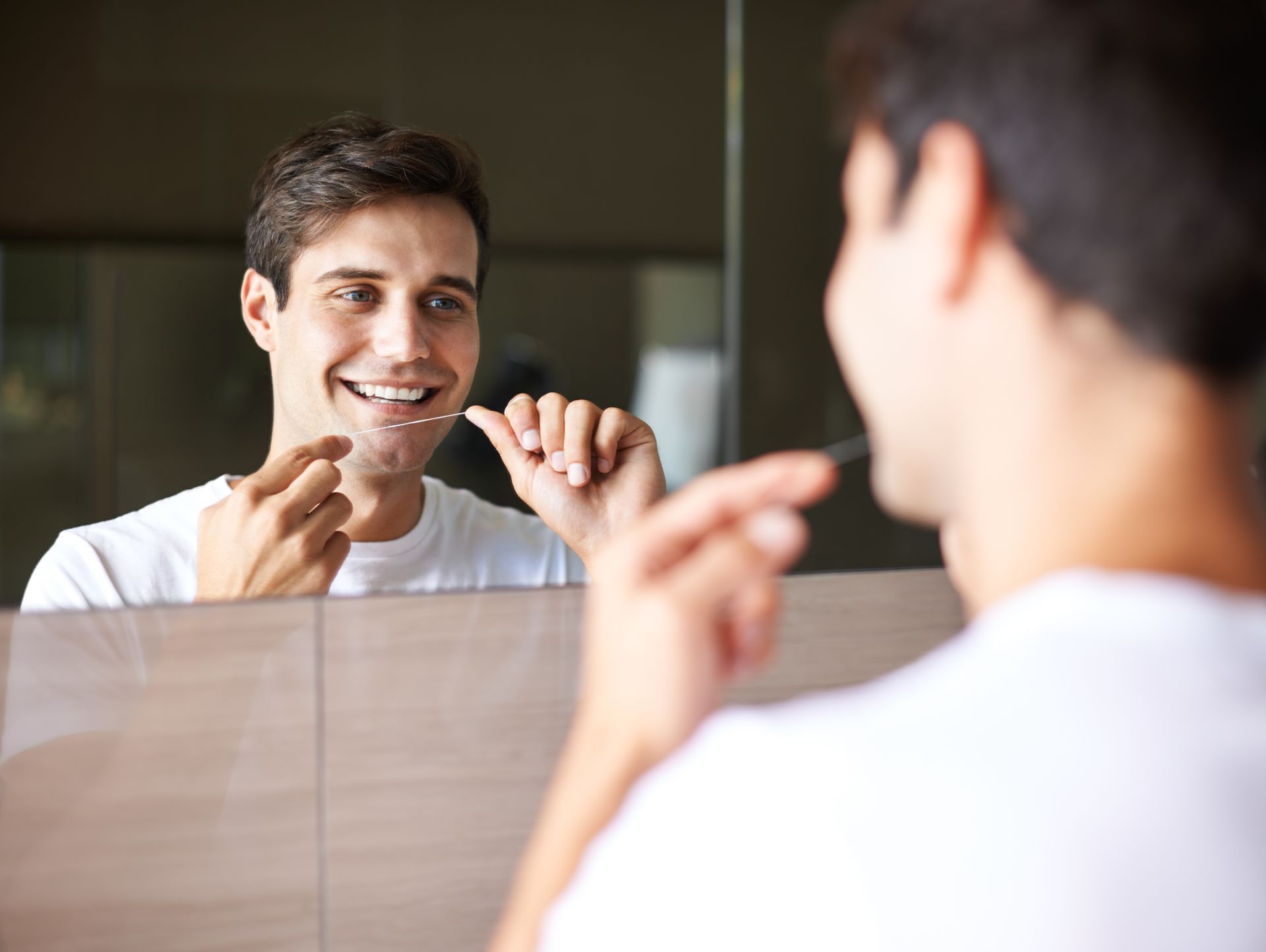 guy in white shirt flossing in front of the mirror