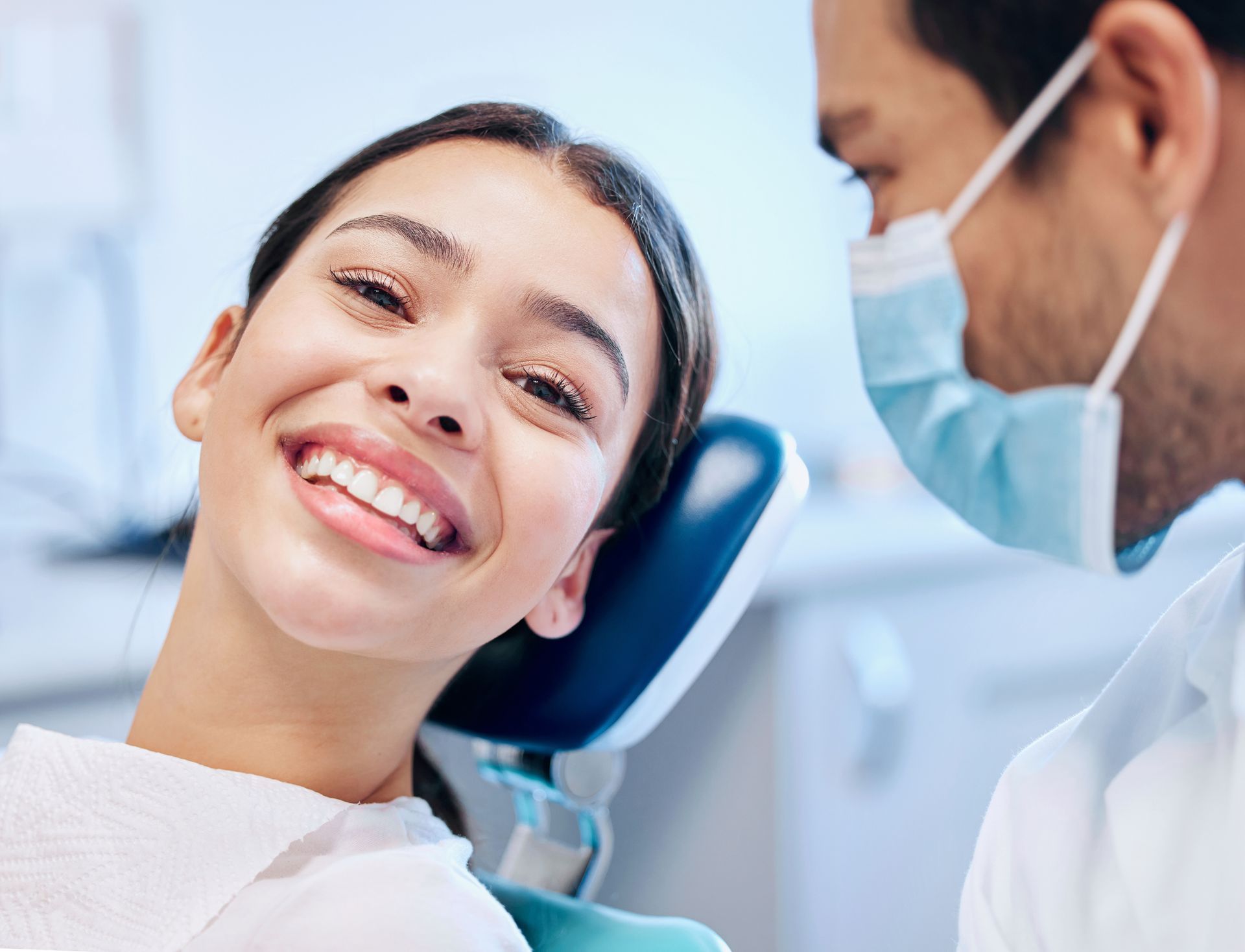 Young female patient smiling confidently in a Wilsonton Heights dental clinic after a cosmetic dentistry consultation with a friendly male dentist wearing a surgical mask