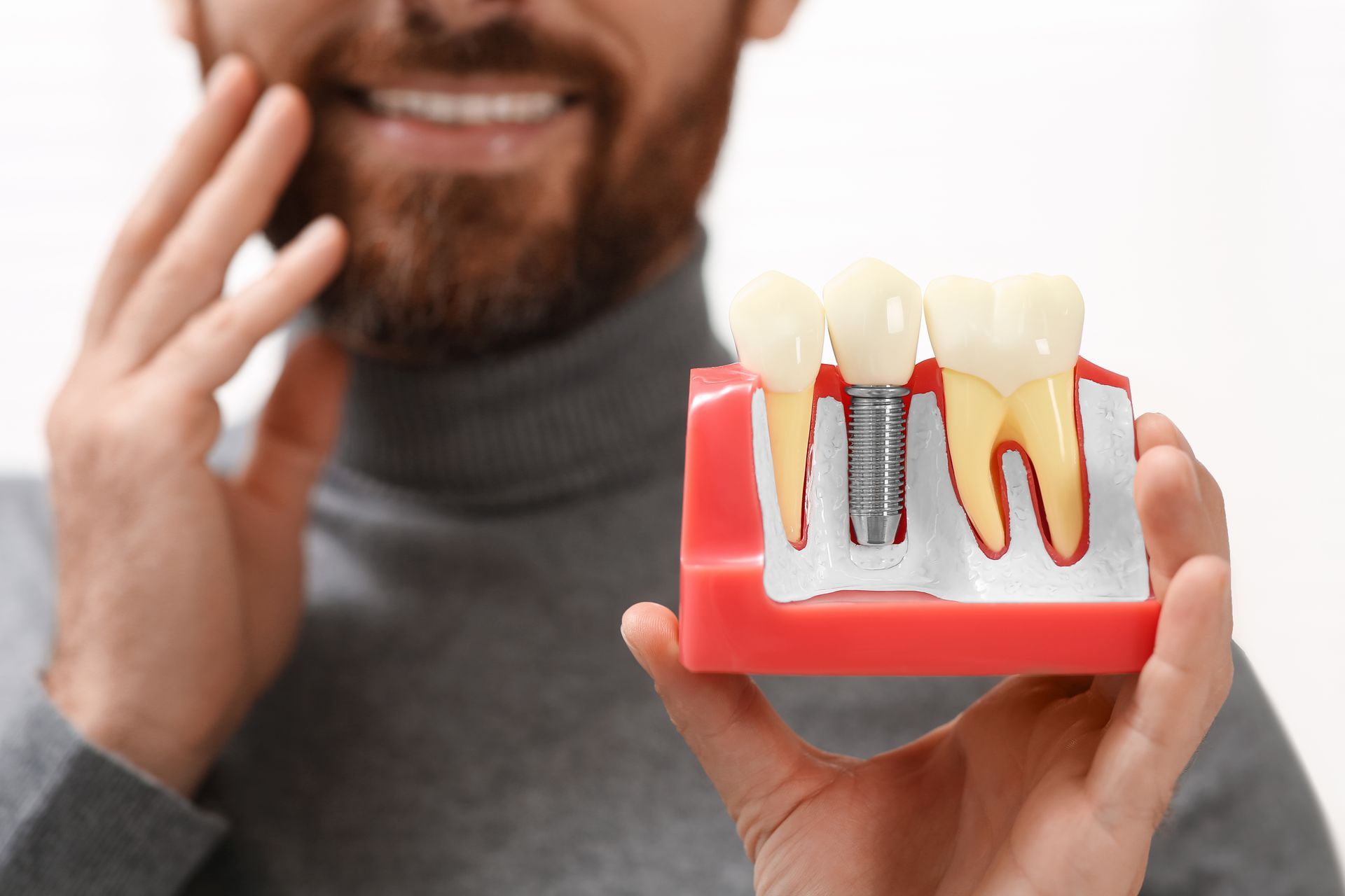 Close-up of a smiling man in Toowoomba holding a dental implant model