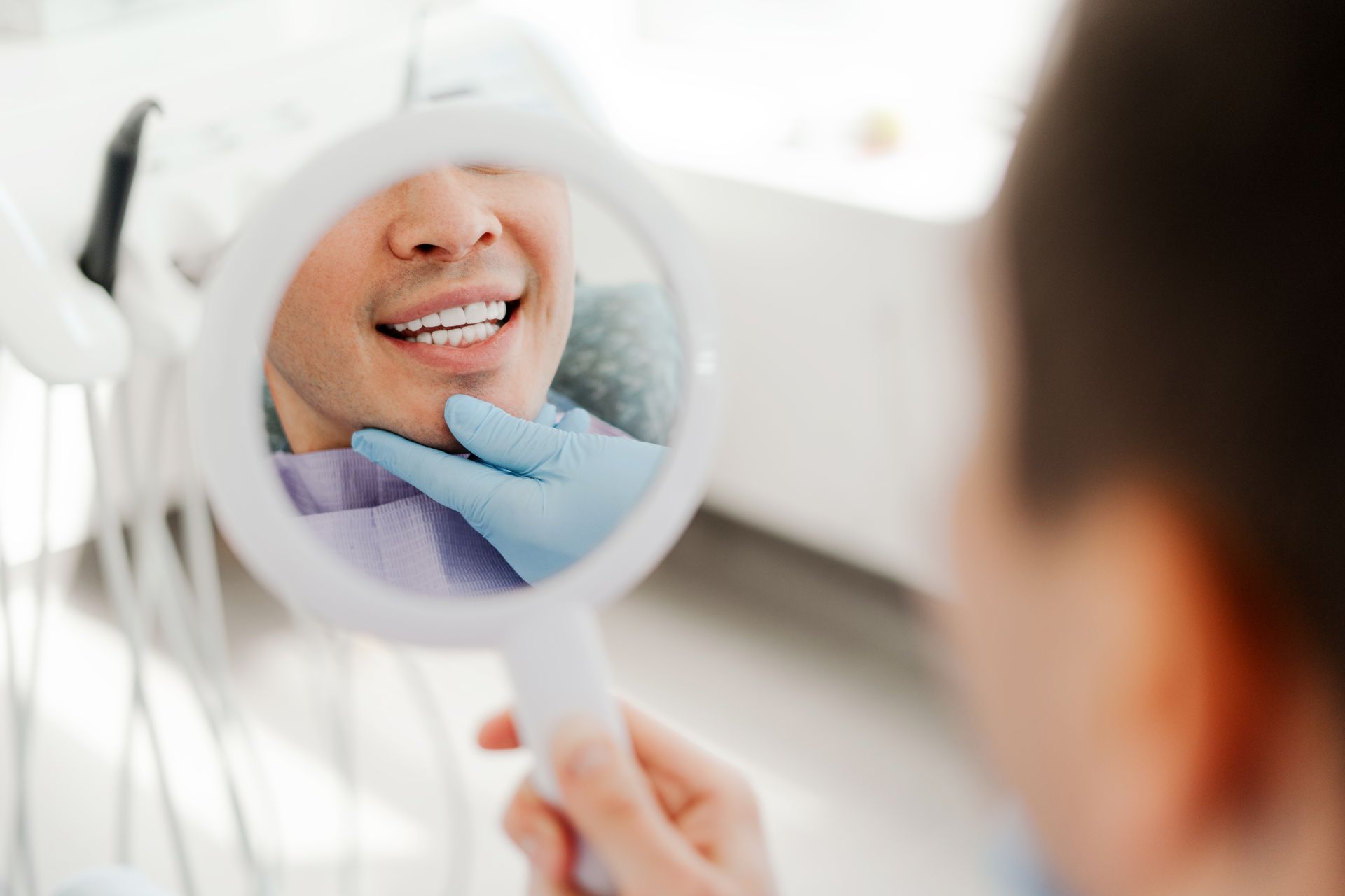 Patient looking at teeth in a mirror while a dentist checks the appearance of the smile.