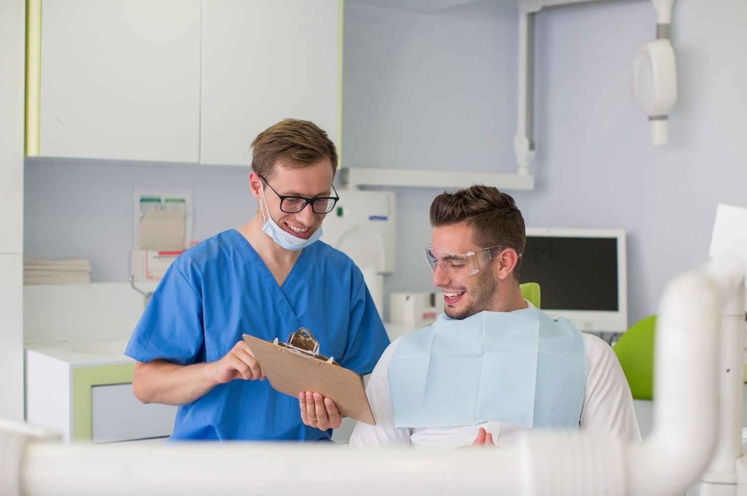 happy male dentist with patient talking at dental clinic office