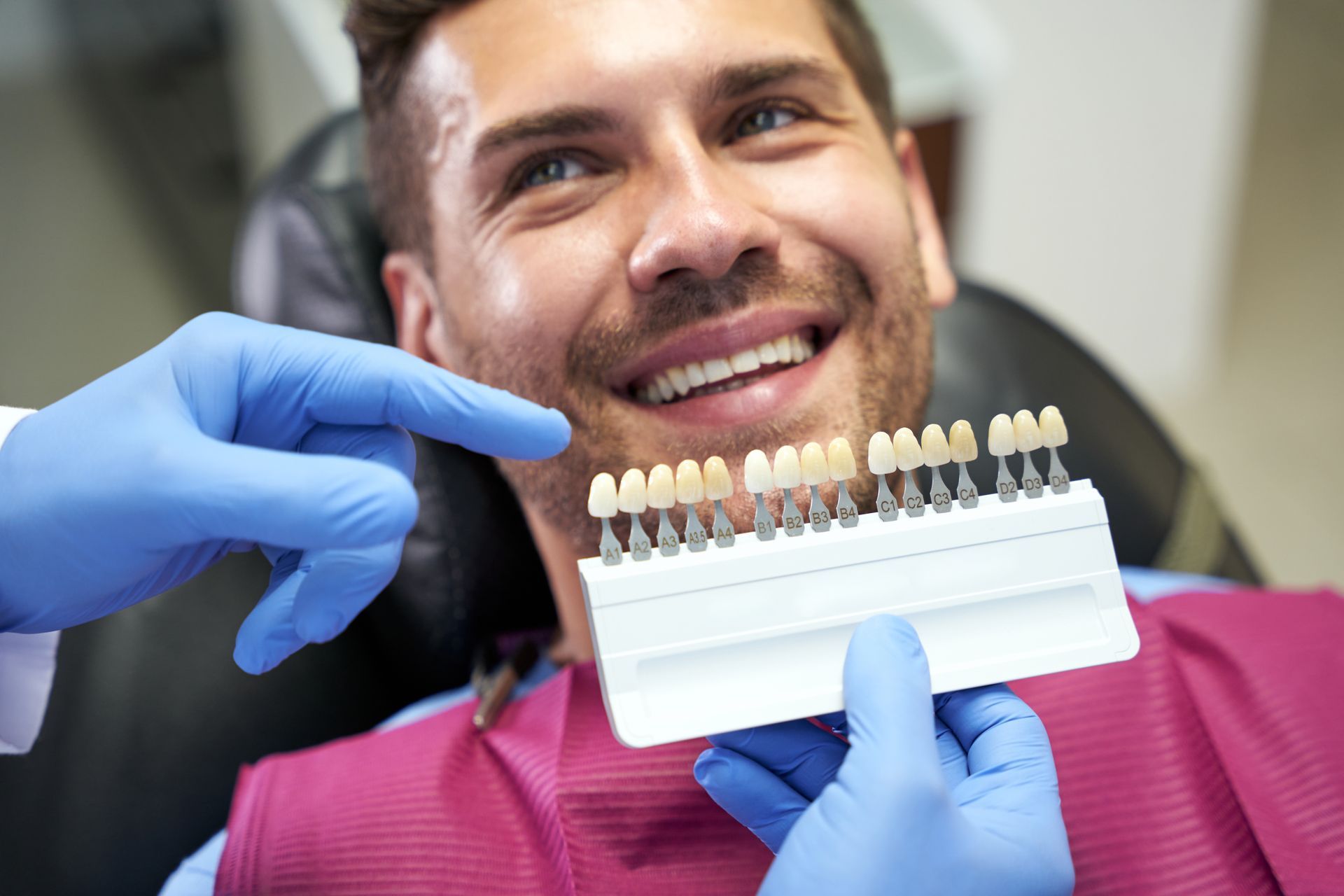 A dentist comparing tooth shade samples to a man's teeth, ensuring the perfect match for his new porcelain veneers