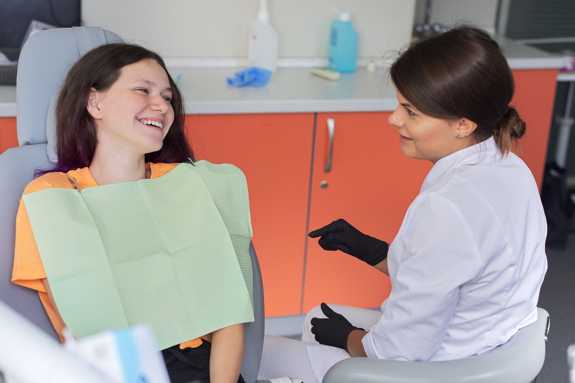 Girl patient in orange shirt smiling towards her dentist