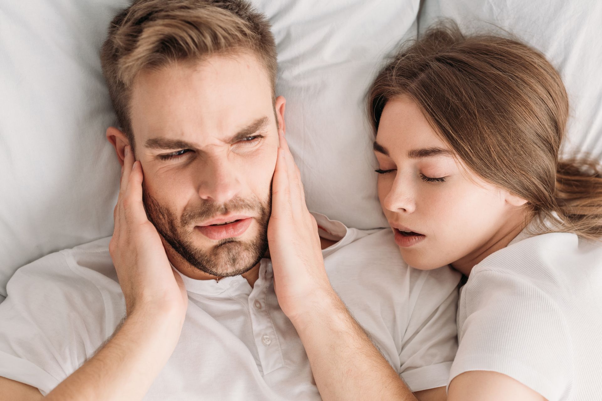 An exhausted man plugging his ears, representing the frustration of sleep apnoea symptoms, treated at Garden City Dental Practice in Toowoomba