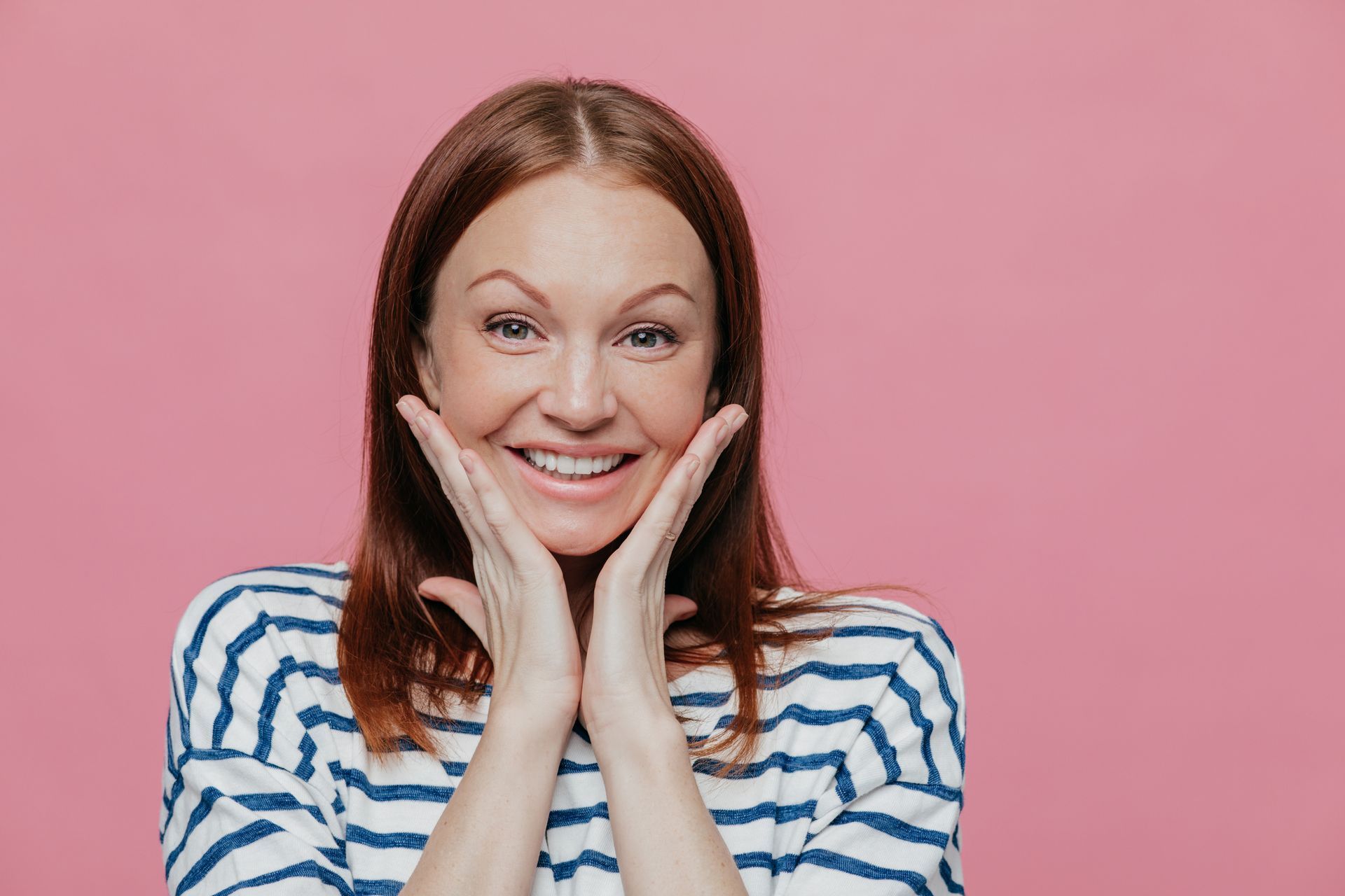 A joyful woman touching her cheeks with her palms, smiling brightly to showcase her new porcelain veneers