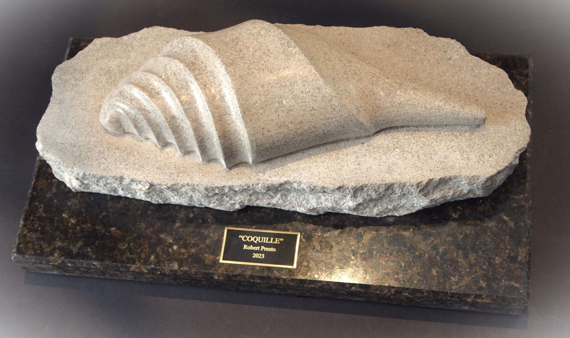 A sculpture of a conch shell on a black granite base