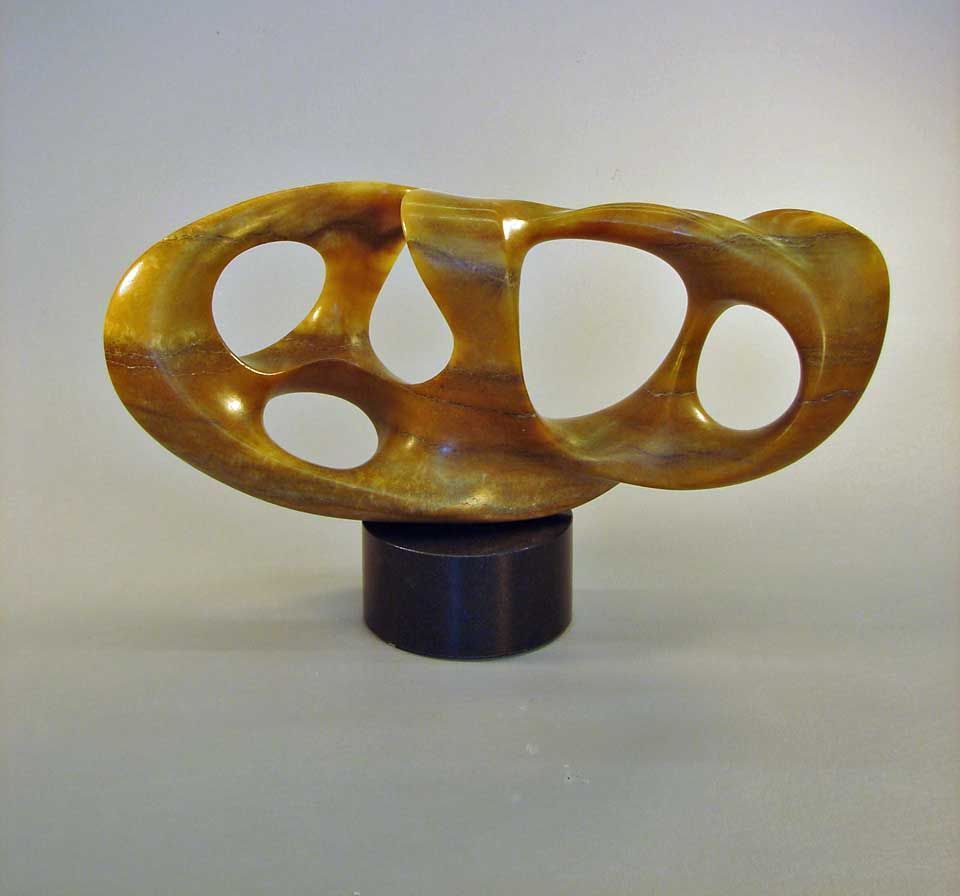 A wooden sculpture with holes in it sits on a black base