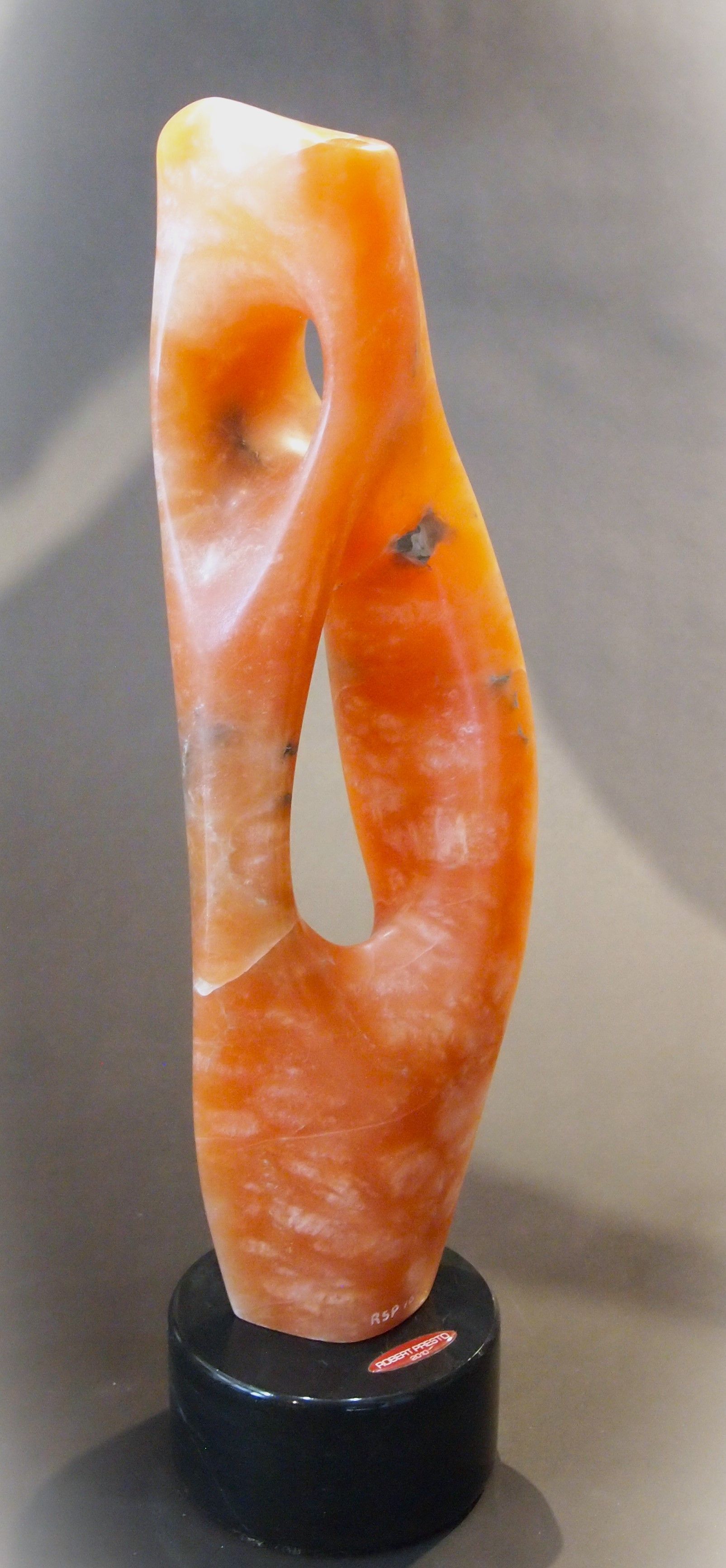 A small orange sculpture is sitting on a black base on a table.