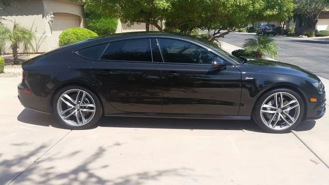 Black sedan parked in a driveway, side view under bright sunlight.