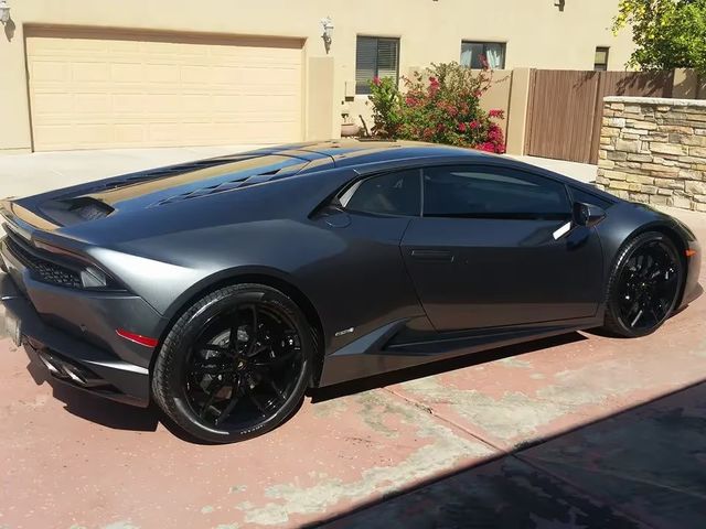 Gray sports car parked in a driveway beside a garage, seen from the rear side.