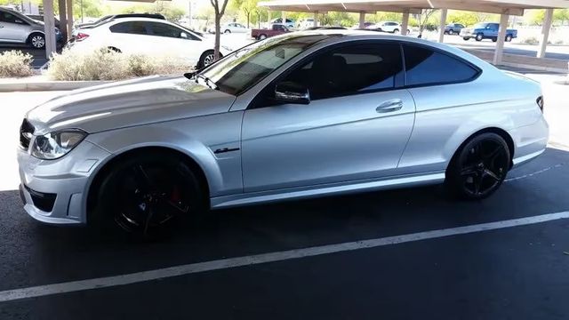 Silver sports coupe parked in a shaded lot, side view with black wheels and tinted windows