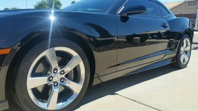 Black sports coupe parked on a driveway, side view with silver rims and bright sun glare on the hood