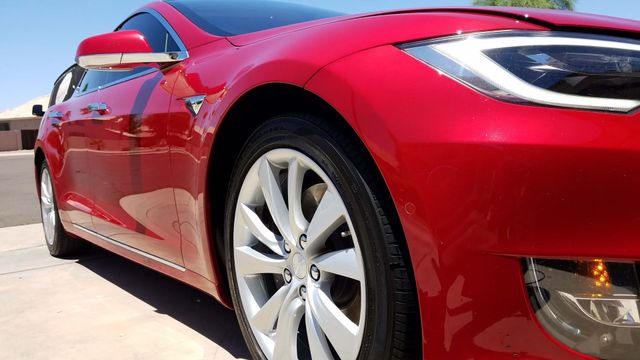 Red sports car parked outdoors, close-up side view with silver wheel and front headlight.